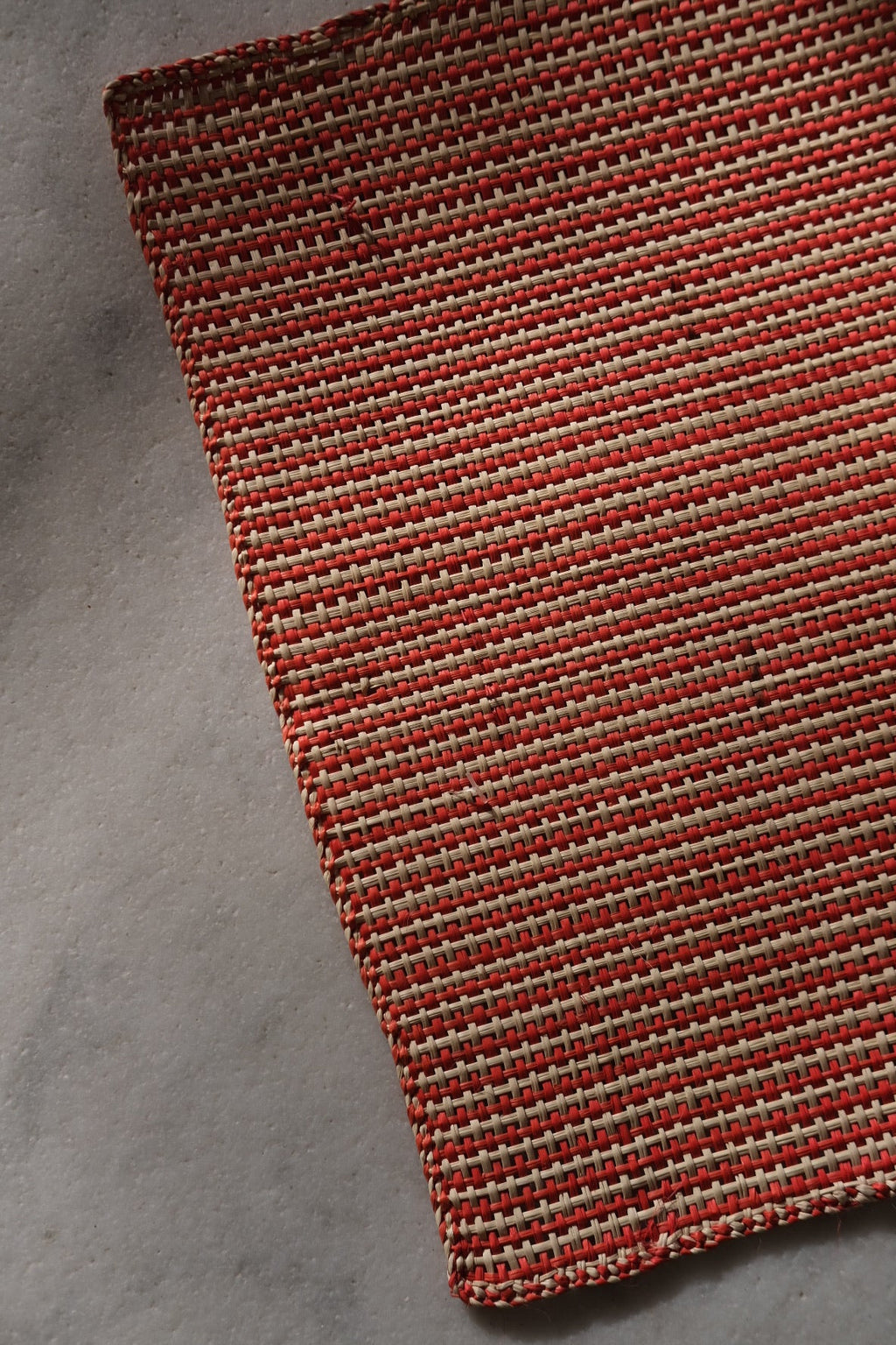 Iraca placemat with red and natural palm leaf design from Guanabana, showcasing vibrant colors and intricate pattern.