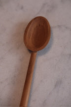 Rød ske i teaktræ, 20 cm, køkkenredskab fra Kunst og Køkkentøj, vises med naturlig trætekstur og håndtag.