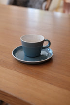 Blå kop og underkop fra ACME Roman Kōkako-serien med elegante, håndlavede keramiske design.