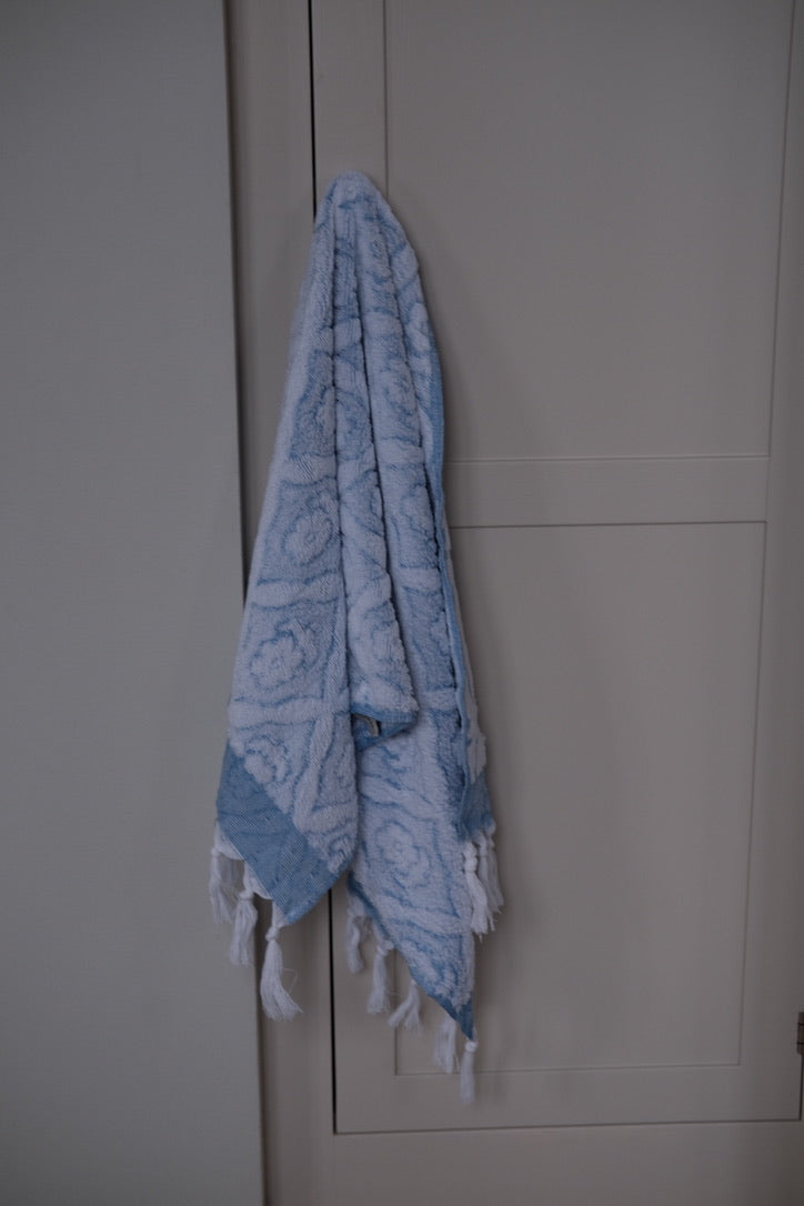 Blue DORA hand towel, 100x50 cm, displayed folded with soft fabric texture on a neutral background.