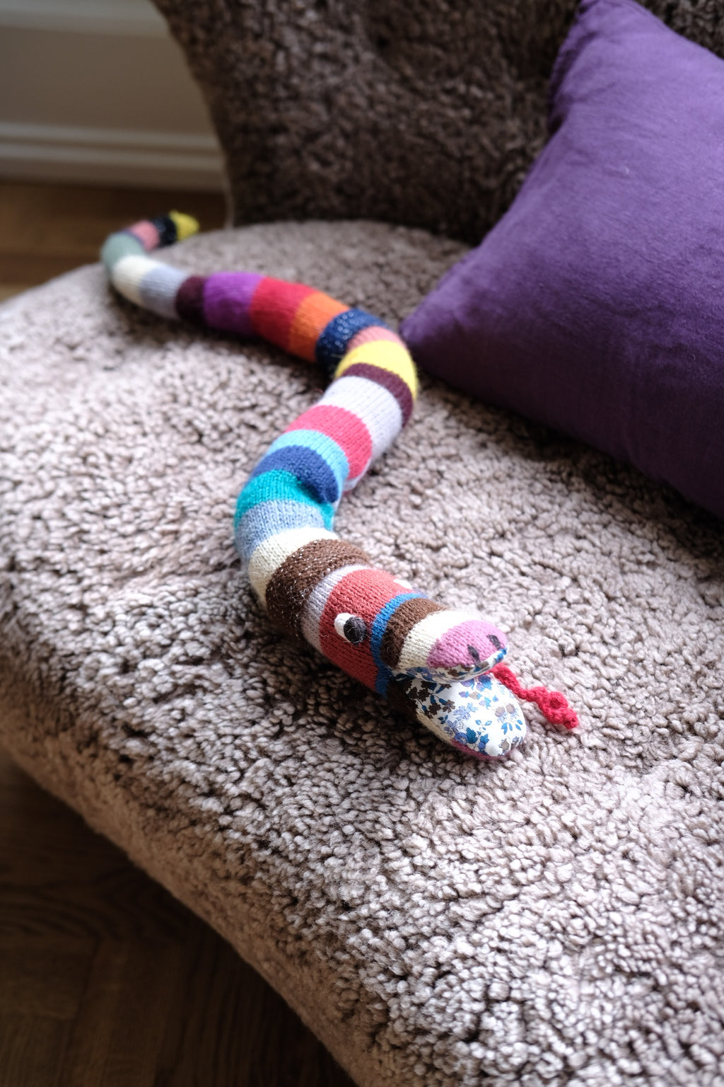 Soft knitted cuddle pillow in snake shape from Creme de la Creme de la Helle, featuring colorful, textured yarn for cozy comfort.