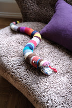 Soft knitted cuddle pillow in snake shape from Creme de la Creme de la Helle, featuring colorful, textured yarn for cozy comfort.