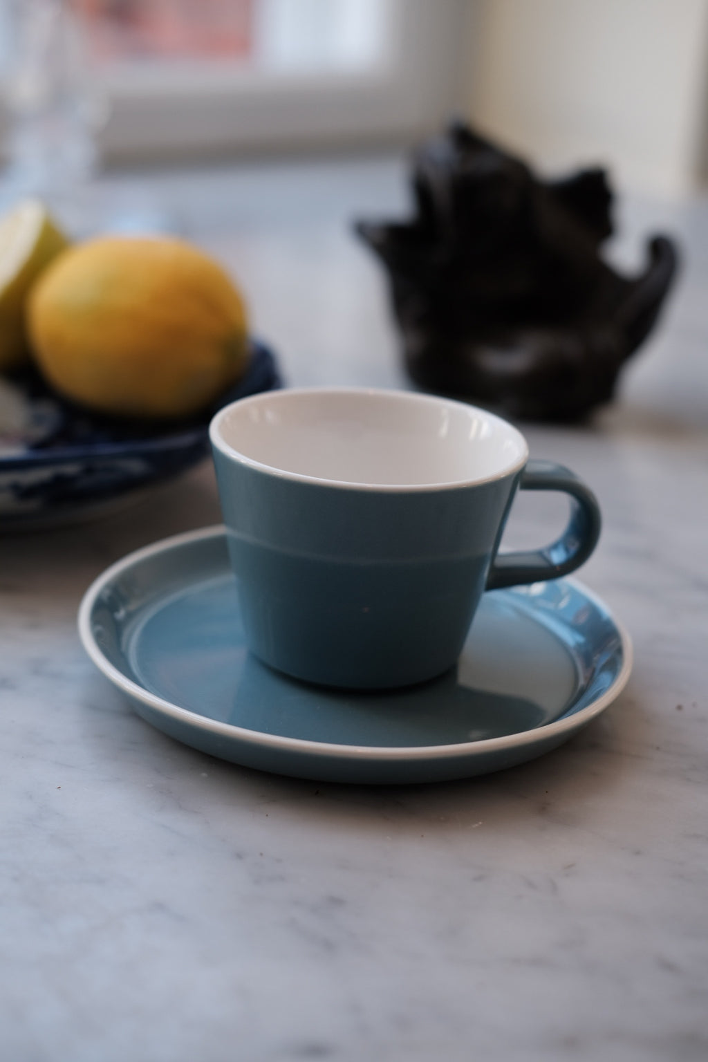 Blå kop og underkop i Acme Roman Kōkako serie, keramisk design med elegant mønster og detaljer.