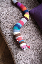 Soft knitted snake-shaped pillow from Creme de la Creme de la Helle, featuring a playful rangle design, perfect for cozy decor.