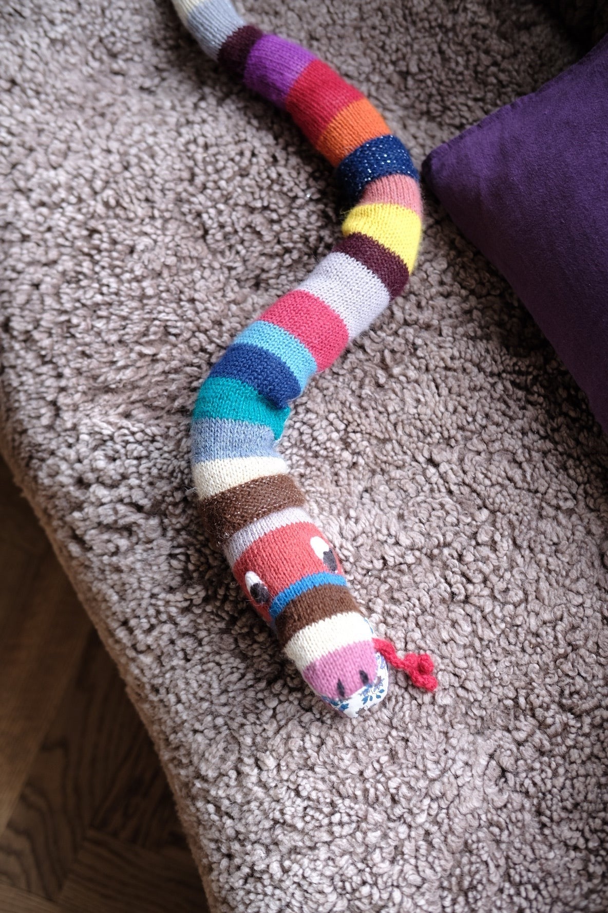 Soft knitted snake-shaped pillow from Creme de la Creme de la Helle, featuring a playful rangle design, perfect for cozy decor.