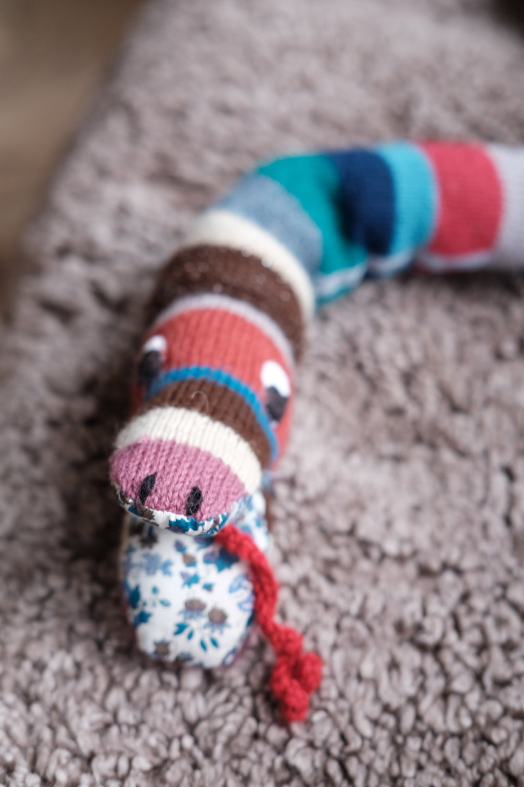 Cream-colored knitted snake-shaped rangle pillow by Creme de la Creme de la Helle, featuring a soft, textured knit design.