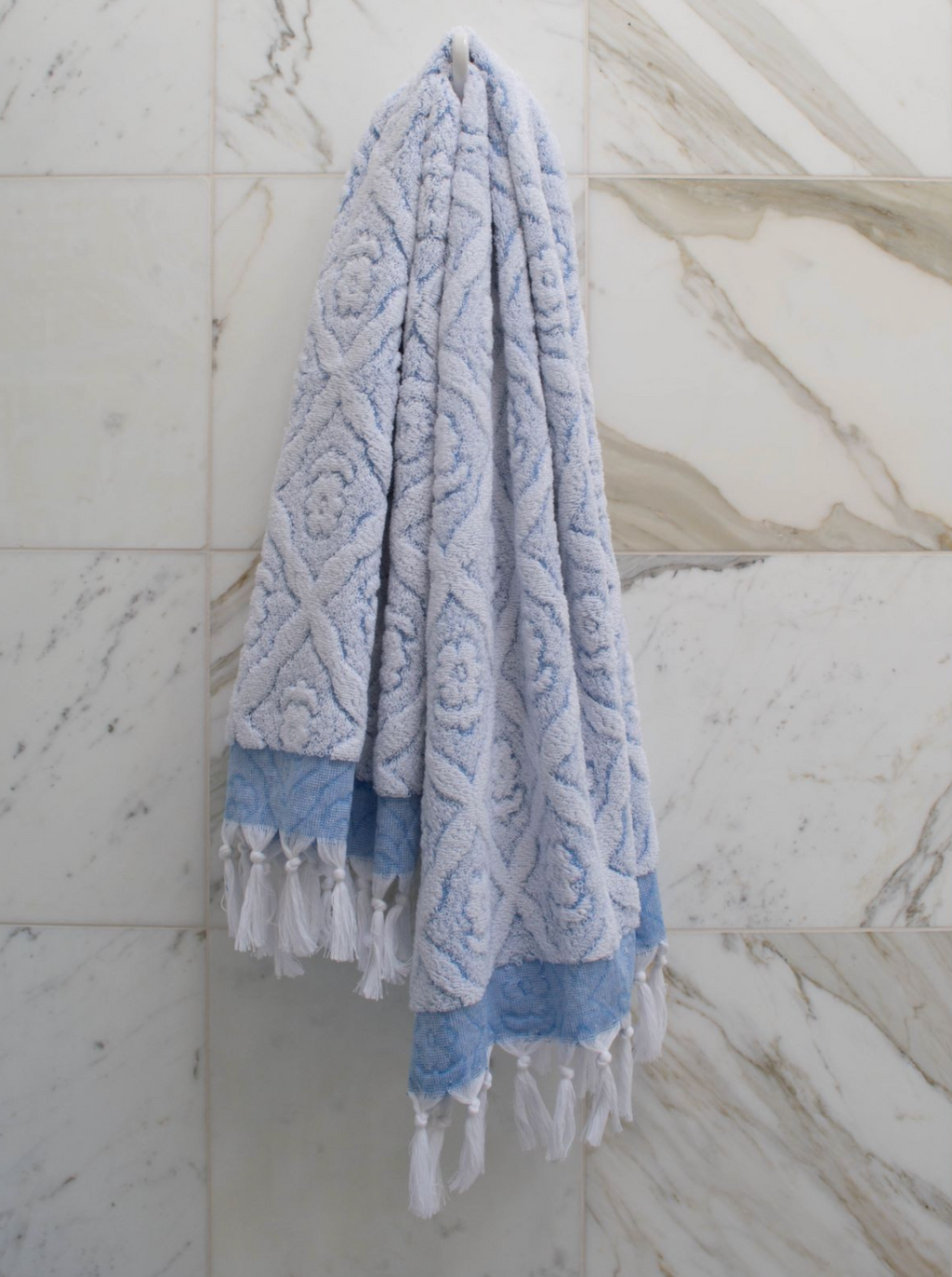 Blue DORA hand towel, 140x70 cm, soft and absorbent, shown draped on a bathroom hook.
