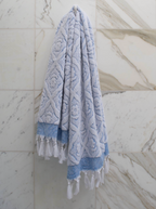 Blue DORA hand towel, 140x70 cm, soft and absorbent, shown draped on a bathroom hook.